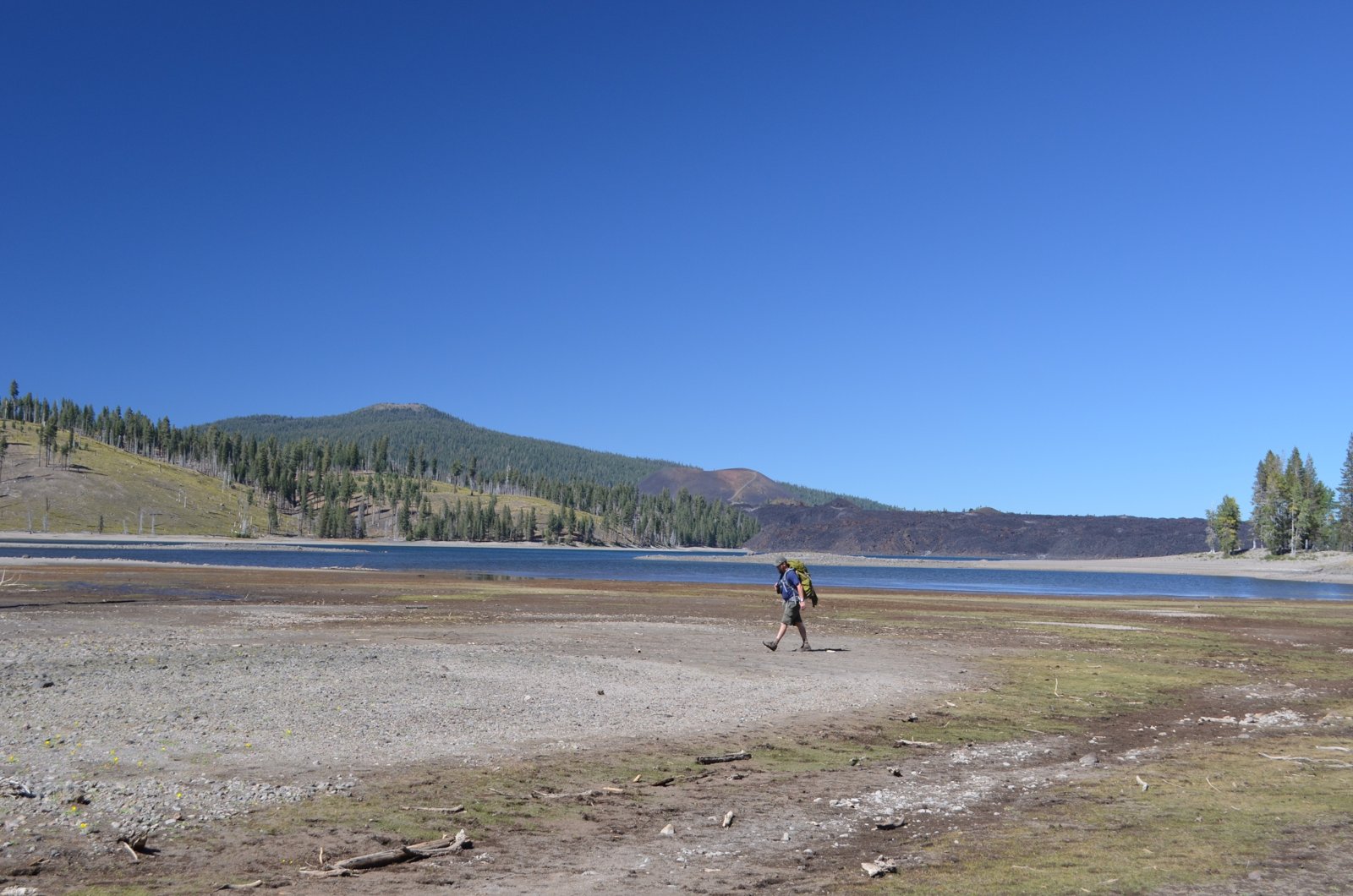 A backpacker on the shore of Snag Lake, with Cinder Cone behind